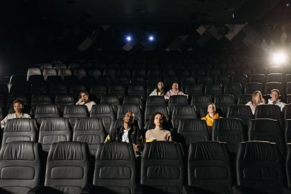 Público diverso, distribuído pela sala escura, assiste a um filme no cinema.