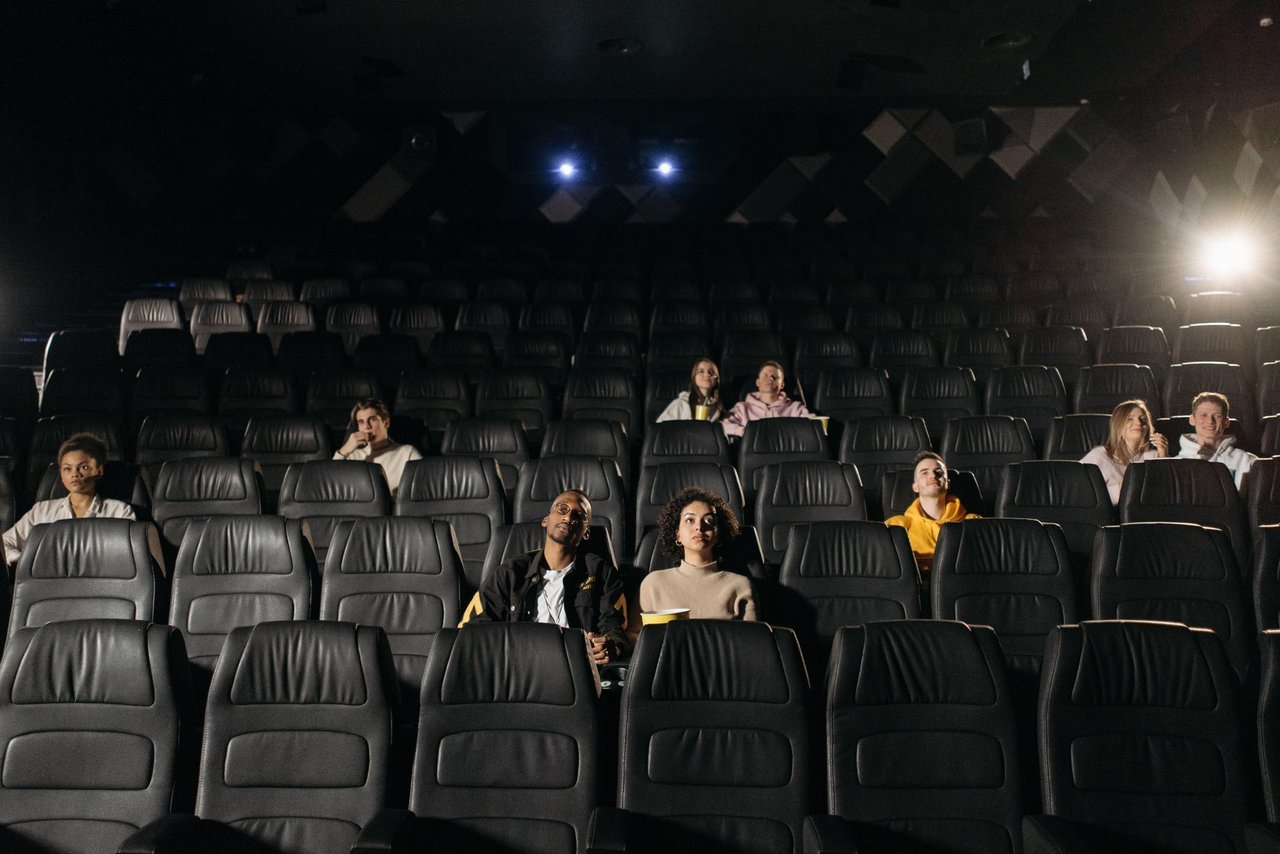 Público diverso, distribuído pela sala escura, assiste a um filme no cinema.