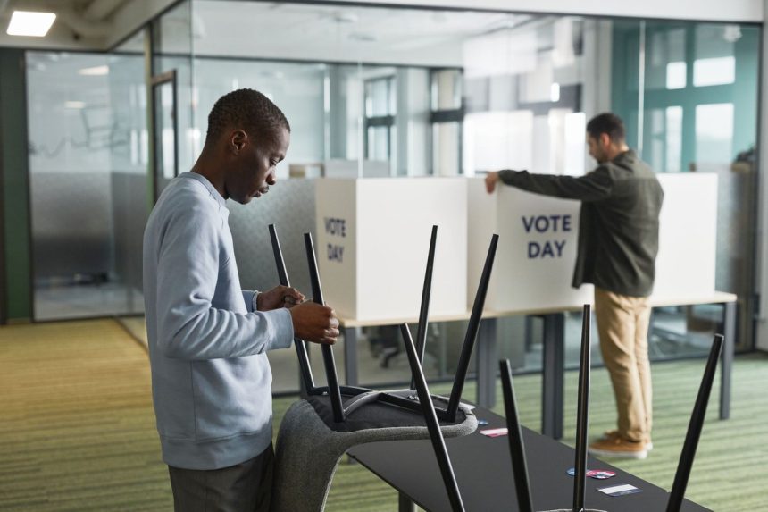 Homens preparam cabines e materiais de votação em um ambiente interno.