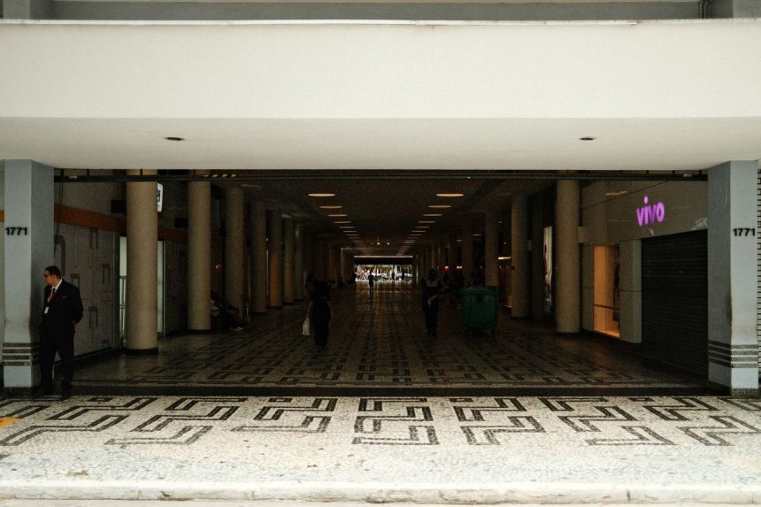 Corredor amplo de um shopping center moderno, com pessoas caminhando sob iluminação interna.