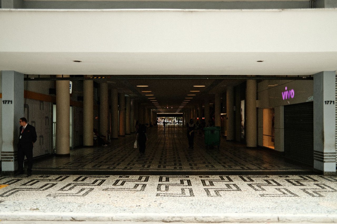 Corredor amplo de um shopping center moderno, com pessoas caminhando sob iluminação interna.