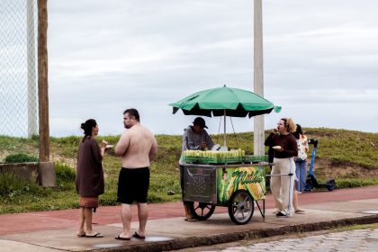 Vendedor comercializa espigas de milho em uma barraca de rua, sob um céu nublado.