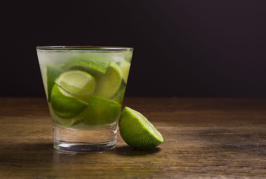 Caipirinha brasileira com limão e cachaça servida em um copo, acompanhada de uma garrafa.